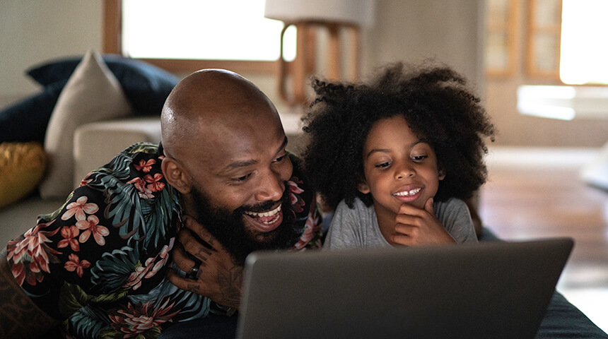 An adult and a child smile at a laptop computer