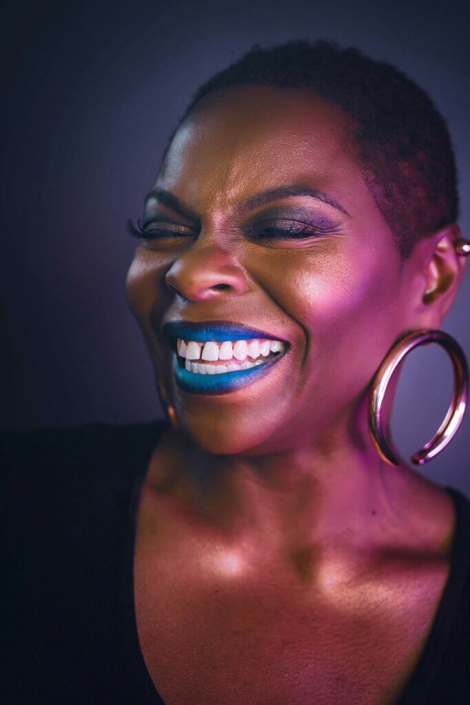 Photo of smiling woman with blue lipstick and large gold hoop earrings.