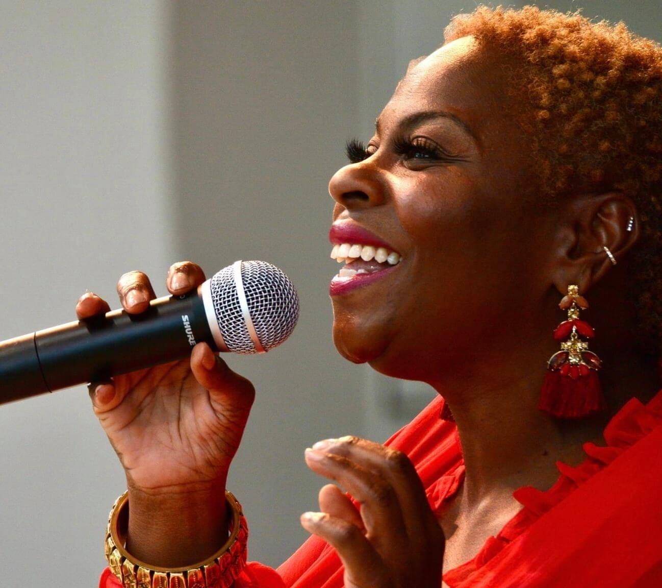 Photo of Anita Levels. Singer with large earrings is holding a microphone to her mouth and smiling.